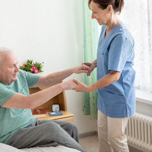 healthcare worker assisting old man out of bed
